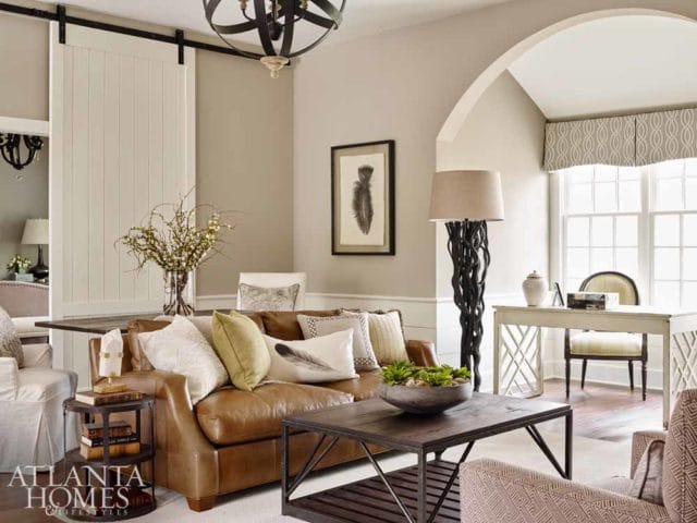 Living room with a brown leather sofa, dark wood coffee table, and a desk with a chair. A large sliding barn door is visible on the left.