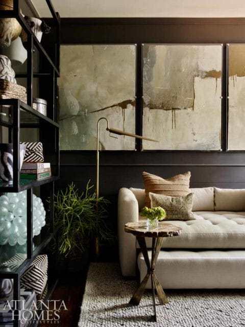 Living room with a tufted cream sofa, abstract art, and a black metal bookshelf filled with decorative items and books.