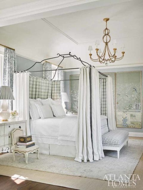 Bedroom with a white canopy bed, plaid and floral curtains, a gold chandelier, and decorative wall panels.