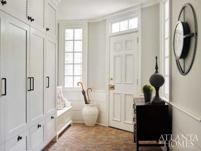 Entryway with white built-in cabinetry, a white paneled door, a dark wood dresser, and a round wall clock.