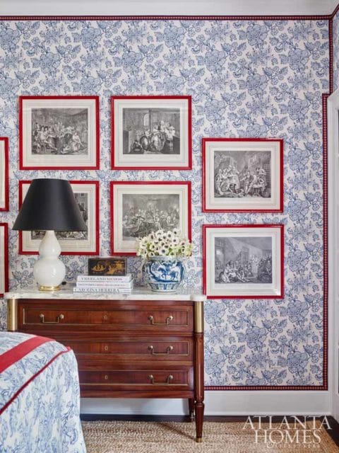 Bedroom with blue and white floral wallpaper, a mahogany dresser with a marble top, and framed antique prints with red borders.