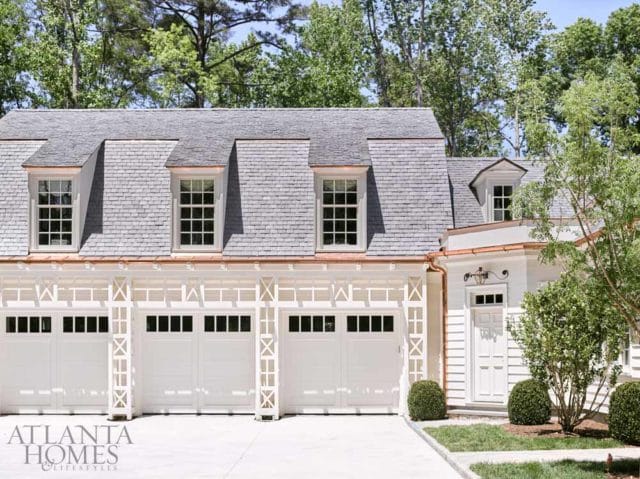 White garage with four doors and dormer windows under a gray shingle roof with copper gutters. A white door is to the right.