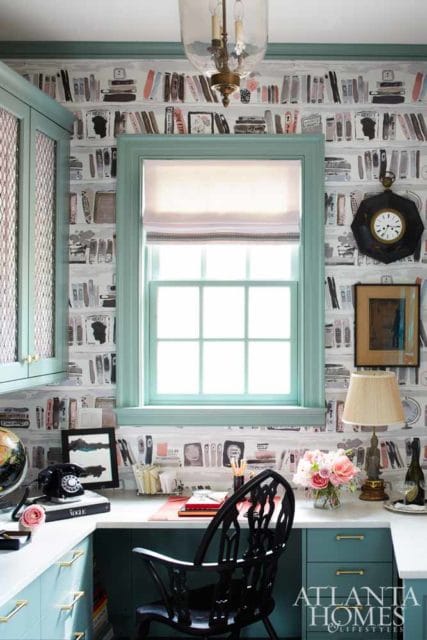 Home office with teal cabinetry, a desk featuring a vintage rotary phone and a Vogue book, and wallpaper with a book pattern.