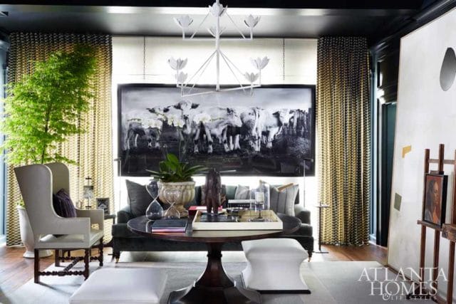 Living room with a large black and white photograph of cows above a dark sofa, a round wooden coffee table with hourglasses, and a wingback chair.