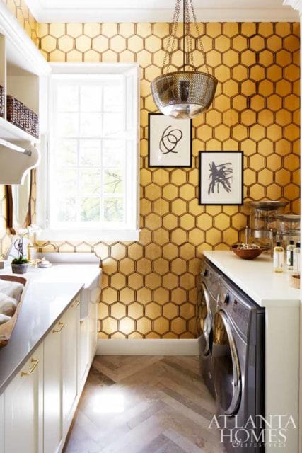 Laundry room with gold honeycomb wallpaper, white cabinetry, white countertop, stainless steel washer and dryer, and herringbone wood floors.
