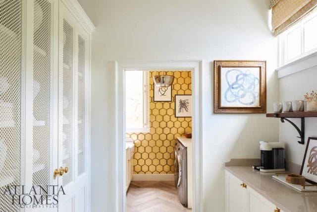 White laundry room with white lattice cabinets, yellow honeycomb wallpaper, herringbone wood floor, and a coffee maker on the counter.