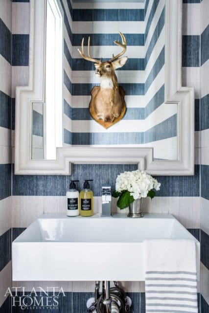 Powder room with blue and white striped wallpaper, a mounted deer head, a white rectangular sink, and a chrome faucet with a vase of white hydrangeas.
