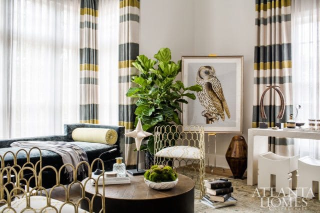 Living room with a dark teal chaise lounge, gold accent chairs, a round wooden coffee table, and a framed owl print.