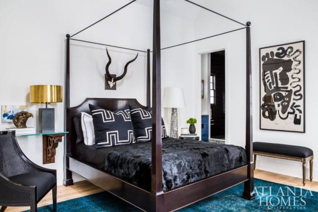 Dark wood four-poster bed with black fur throw and graphic black and white pillows. Antlers mounted on wall above bed.
