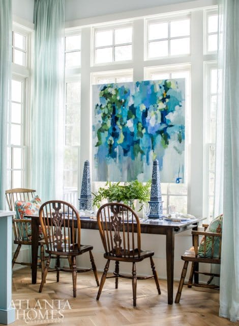 Dining room with dark wood table and chairs, light blue curtains, and a large abstract painting with blue and green tones above the table.