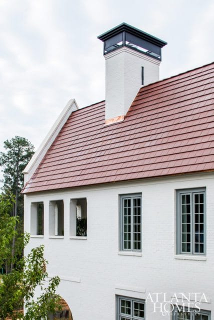 White brick house with a red tile roof, a tall white brick chimney with a black cap, and grey-framed windows.