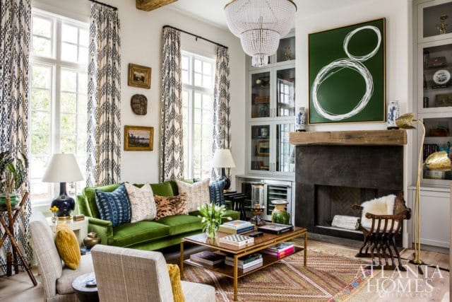 Living room with a bright green velvet sofa, patterned curtains, a dark stone fireplace, and a large abstract green painting above the mantel.