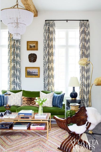 Living room with a vibrant green sofa, patterned curtains, a large beaded chandelier, and a wooden chair with white fur accent.