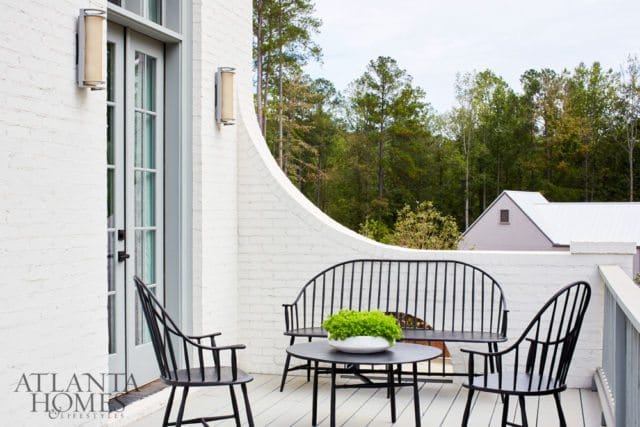 White brick patio with black metal furniture including a bench, two chairs, and a round table with a green plant in a white bowl.