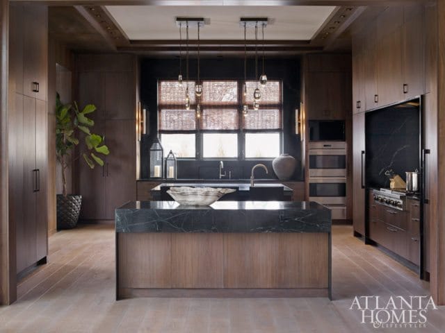Dark wood kitchen with a large marble island, stainless steel appliances, and a large window with woven blinds.