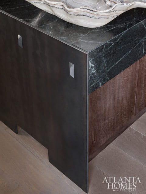 Close-up of a dark marble countertop with a metal base and wood cabinetry, featuring a large decorative bowl on top.