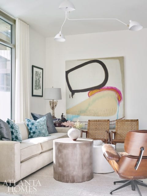 Living room with a cream sofa, abstract art, concrete coffee table, and leather Eames lounge chair.