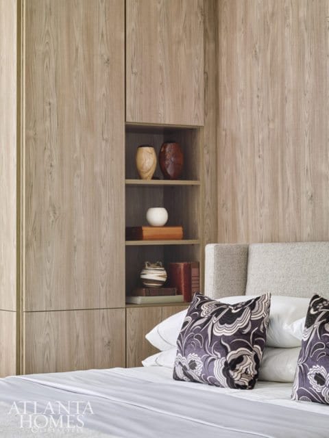 Bedroom with built-in wood-grain cabinetry, open shelving displaying decorative vases and books, and a bed with patterned pillows.