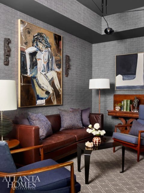 Living room with textured gray walls, featuring a brown leather sofa, blue upholstered armchairs, a large abstract painting of a nude, and a black coffee table.