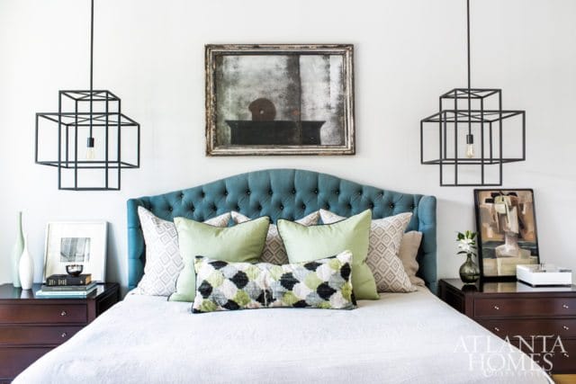 Bedroom with a teal tufted headboard, white linen bedding, sage green and patterned throw pillows, and geometric black pendant lights.