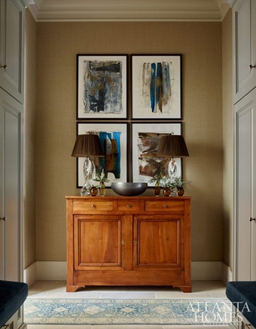 Hallway with textured tan walls, a wooden credenza topped with abstract art and lamps, and a blue and white patterned runner on a stone floor.