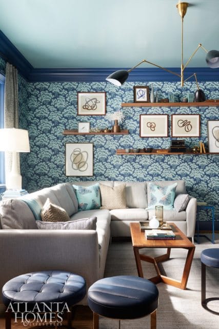 Living room with a sectional sofa, blue tree-patterned wallpaper, and a brass multi-arm chandelier.