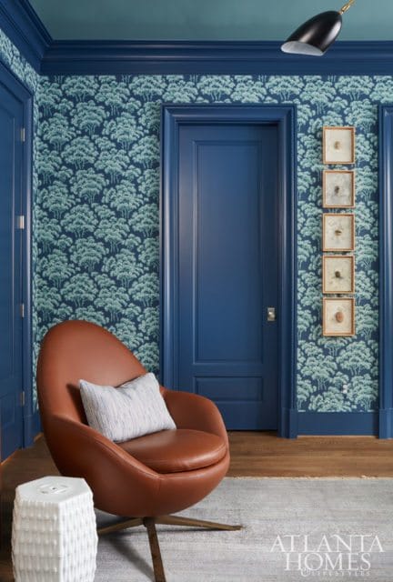 Blue room with tree-patterned wallpaper, a brown leather swivel chair with a striped pillow, and framed insect specimens on the wall.