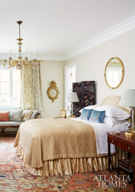 Bedroom with a gold quilted bedspread, blue velvet pillows, ornate chandelier, and a large oriental rug.