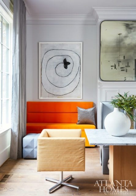 Living room with a bright orange banquette, a yellow armchair with a chrome base, and abstract art on the wall.