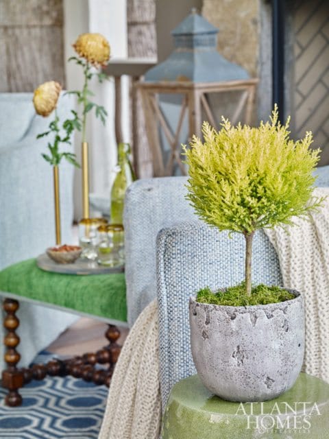 Light blue upholstered chair with a cream knit throw draped over it, next to a green upholstered bench with wooden legs. A small potted plant sits on a green stool in the foreground.