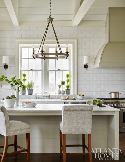 White subway tile backsplash and shiplap walls in a kitchen with a marble island, two upholstered bar stools, and a metal range hood.