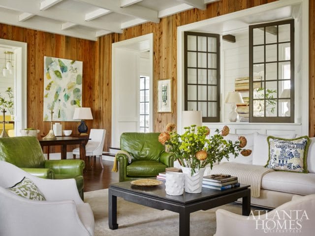 Living room with wood-paneled walls, white coffered ceiling, green leather armchairs, a white sofa, and a dark coffee table with a floral arrangement.