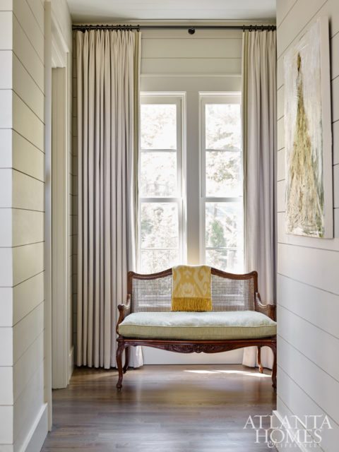 In the master bedroom hallway, a cane-back settee with pretty curves, one of the client’s treasured pieces, was updated in a Pindler fabric and Samuel & Sons trim.