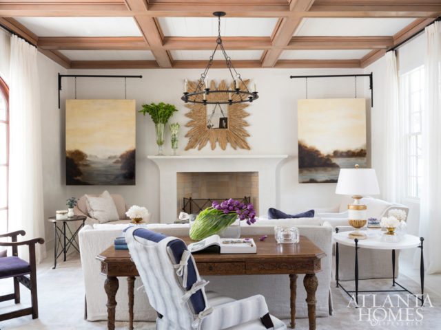In the main living room, a cypress coffered beam ceiling provides warmth and texture. Russ wanted the space to feel comfortable yet orderly, so Turner used a pair of landscape paintings by Charlotte Terrell to conceal the room’s television, while pops of plum reference the homeowners’ family name. Mirror through Design Legacy. Sofa and desk chair through LEE Industries. Desk through Noir. The chandelier is through Currey & Company.