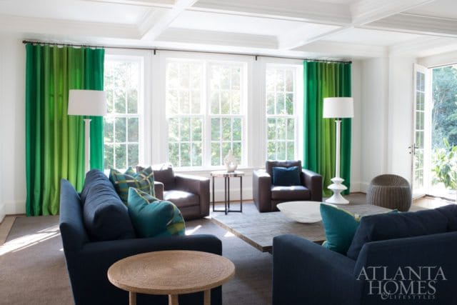 Living room with navy sofas, brown leather armchairs, green ombre curtains, and a coffered ceiling. A large wooden coffee table sits in the center.