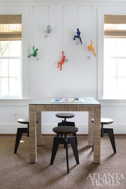 Game room with a table set up for a board game, surrounded by four stools. Colorful climbing figures are mounted on the wall above.