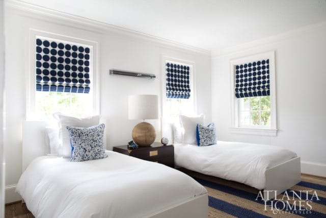 Bedroom with two twin beds, white bedding, navy and white polka dot roman shades, and a striped rug.