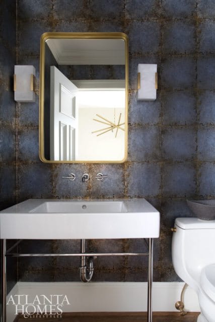 Powder room with dark, textured tile walls, a white rectangular sink on a chrome stand, a gold-framed mirror, and modern sconces.