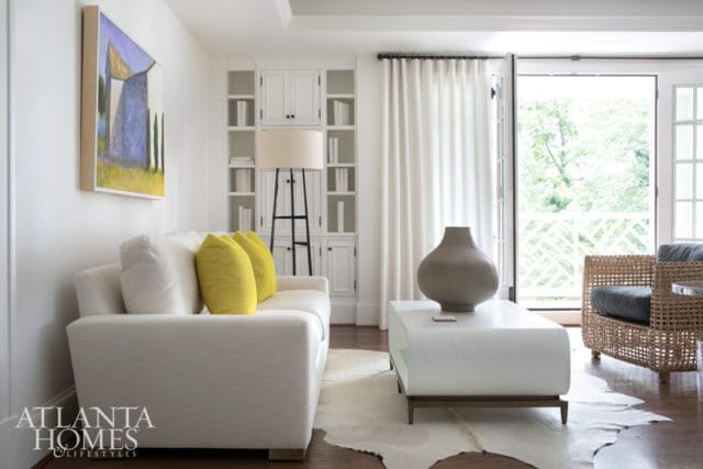 White sectional sofa with yellow accent pillows, white coffee table with ribbed vase, and built-in white shelving unit.