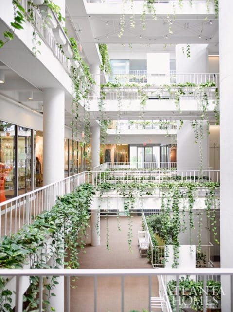 Multi-level interior atrium with white railings and numerous hanging plants cascading down from balconies.