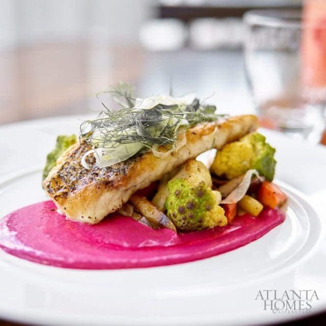Pan-seared fish fillet served with roasted vegetables including cauliflower and carrots, on a swirl of bright pink sauce.