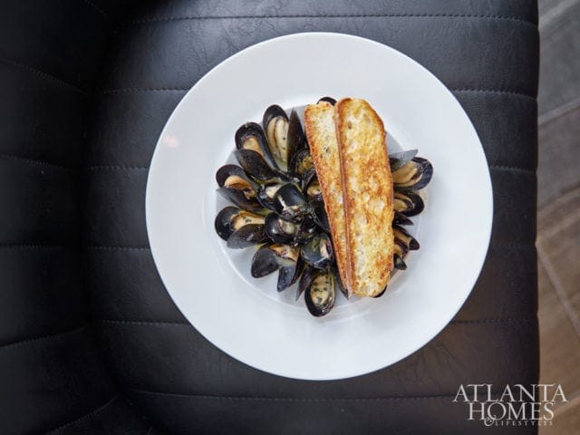 White plate of mussels with two slices of toasted baguette on top, set against a dark textured background.