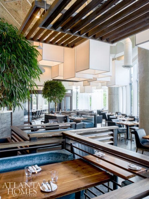 Modern restaurant interior with wood tables, blue upholstered booths, and a slatted wood ceiling with square white pendant lights.