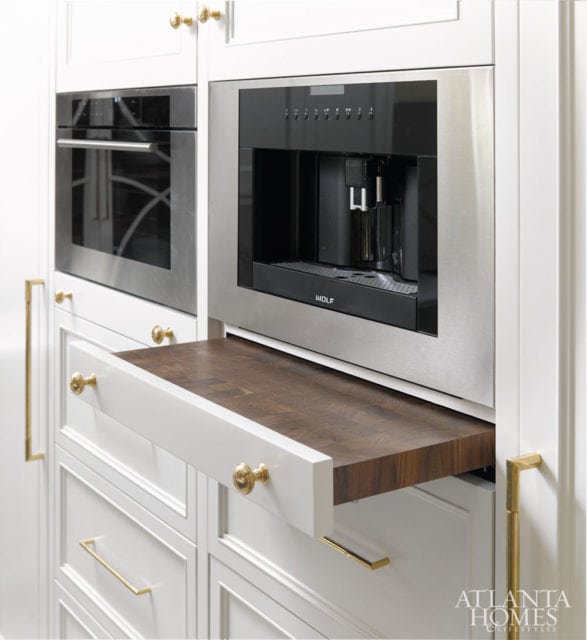 White kitchen cabinetry with a built-in Wolf coffee maker, stainless steel oven, and a pull-out butcher block cutting board.