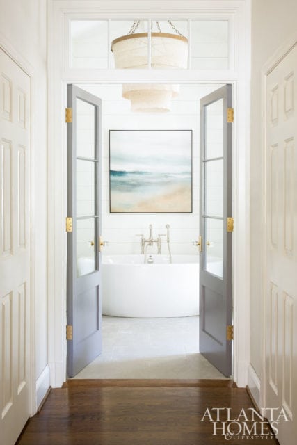 Spa-like bathroom with a freestanding soaking tub, shiplap walls, and a large abstract landscape painting above the tub. Double doors open into the room.