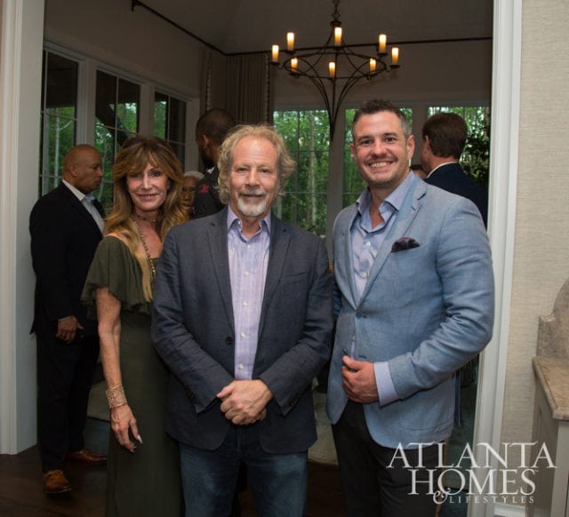 Three people pose for a photo in an interior setting with a chandelier overhead and a logo for Atlanta Homes & Lifestyles in the lower right corner.