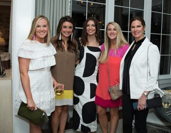 Five women in dresses and jackets pose for a photo indoors.