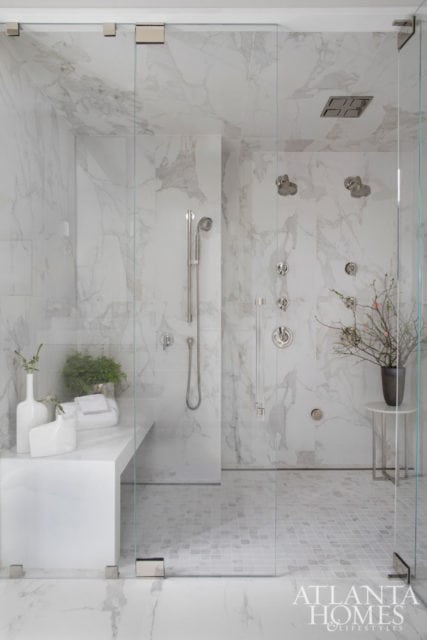 Modern white marble bathroom with a glass-enclosed shower featuring multiple showerheads, a built-in bench, and mosaic tile flooring.