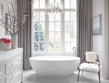 White bathroom with freestanding tub, double vanity, and fur-covered chair.