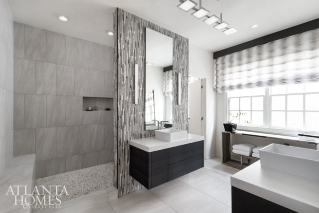 Modern bathroom with large format gray stone tiles on the shower walls and floor, a floating dark wood vanity with a white vessel sink, and a large mirror with a decorative vertical striped surround.